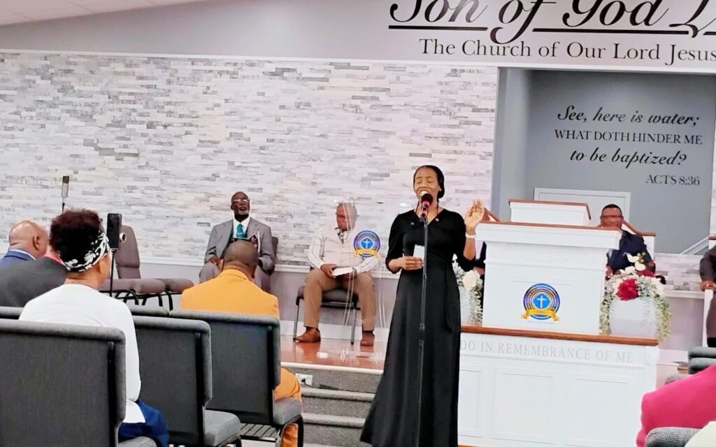 A woman sings passionately into a microphone at a church service, while congregation members listen attentively from their seats.