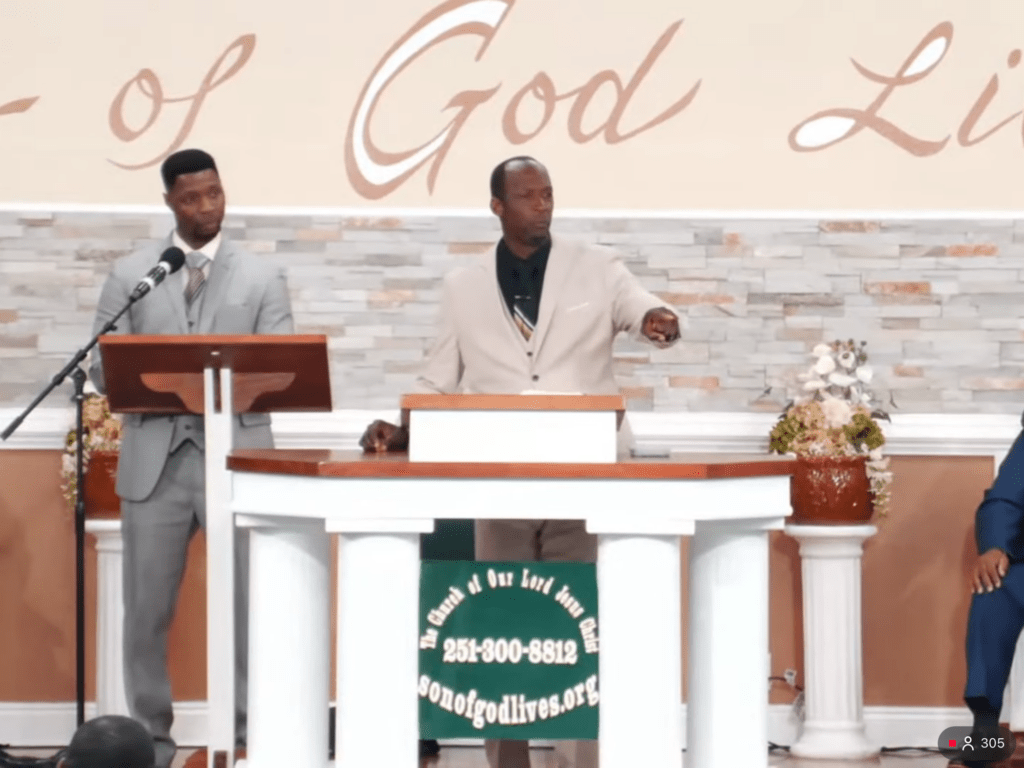 Two men speak at a church podium, one gesturing as he addresses the audience, while the other listens intently. The setting emphasizes community worship.