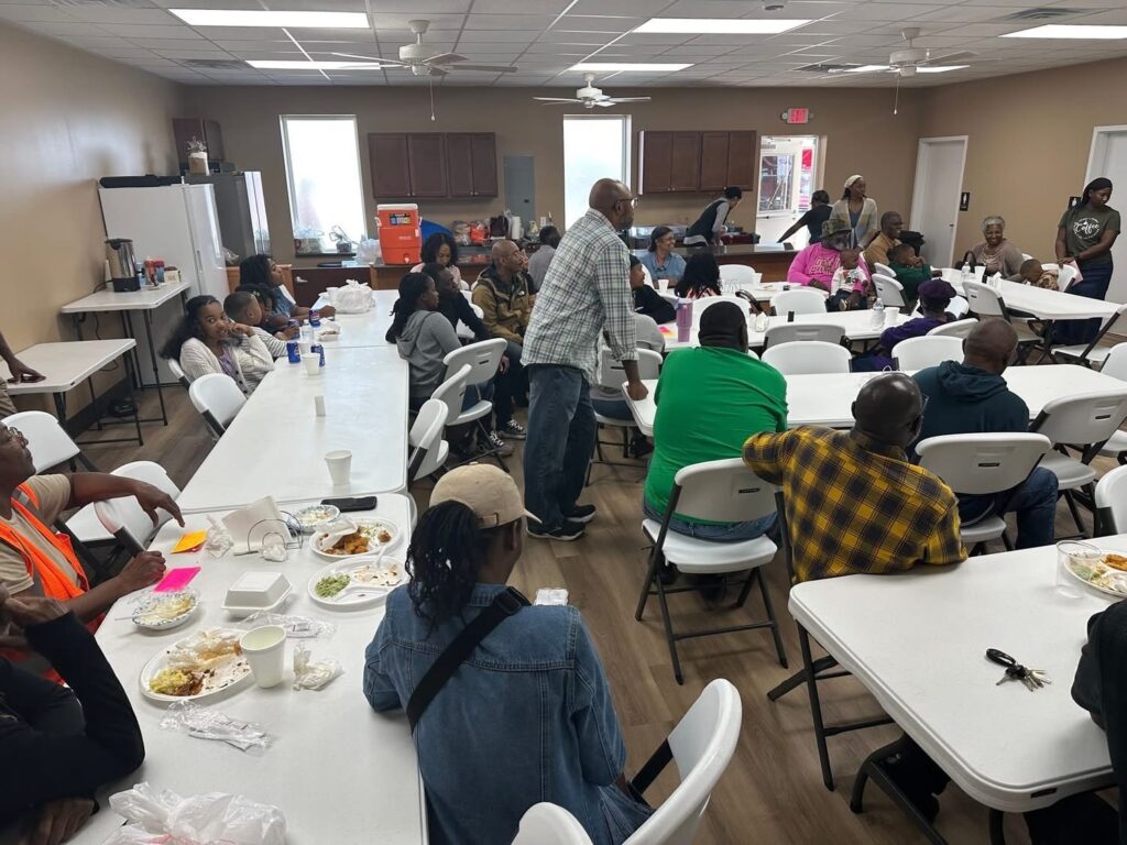 Community gathering in a dining hall. Attendees share a meal while engaging in conversation, highlighting the social aspect of the event.